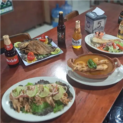 Mesa servida con gran variedad de platillos de mariscos, pescado frito, caldo y cervezas frías en Restaurante Moyo en Martínez de la Torre.