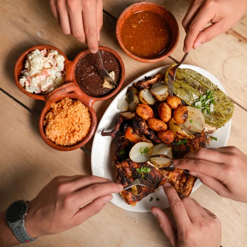 Grupo de personas compartiendo una deliciosa parrillada con carne al carbón, cebollitas asadas y guarniciones tradicionales en Asadero Moyo, Martínez de la Torre.