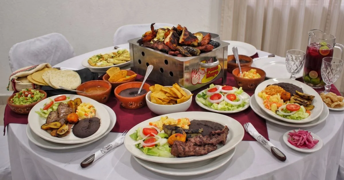Mesa servida con un banquete familiar que incluye una parrillada de pollos al carbón, costillas, guarniciones mexicanas y bebidas frescas en el restaurante Pollo Moyo de Martínez de la Torre.