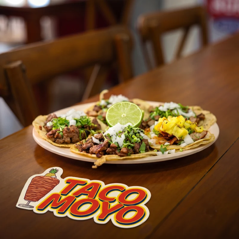 Plato de tacos surtidos recién preparados sobre una mesa de madera junto al logo de Taco Moyo, el mejor restaurante en Martínez de la Torre.